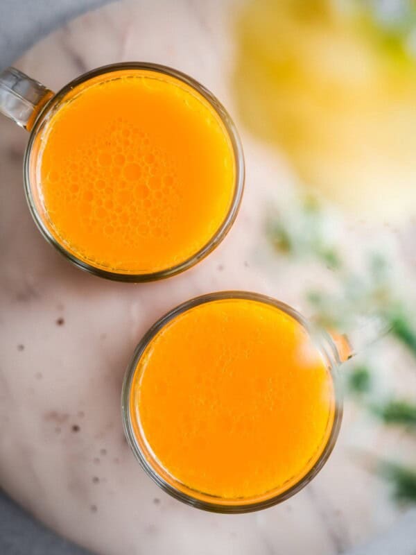 Overhead view of two glasses of turmeric tonic on a marble serving tray.