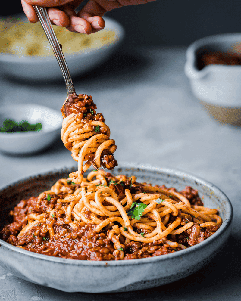 a fork twirling spaghetti in a bowl of red lentil bolognese.