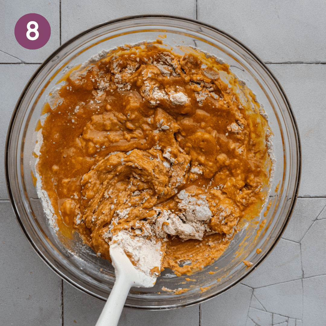 spatula mixing liquid ingredients into dry ingredients for vegan pumpkin bread in a glass bowl.