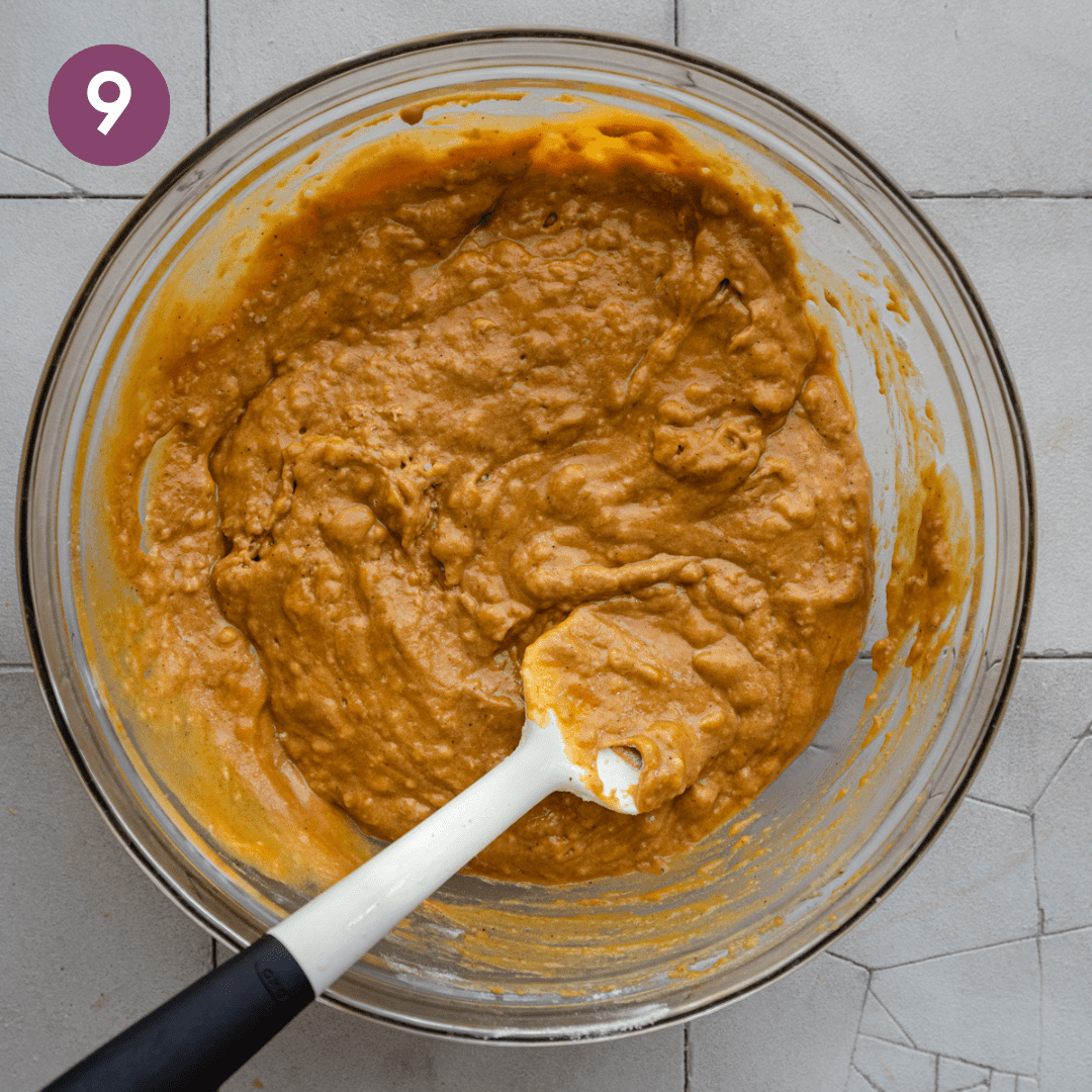 spatula sitting in a bowl of thick pumpkin bread batter in a glass bowl.
