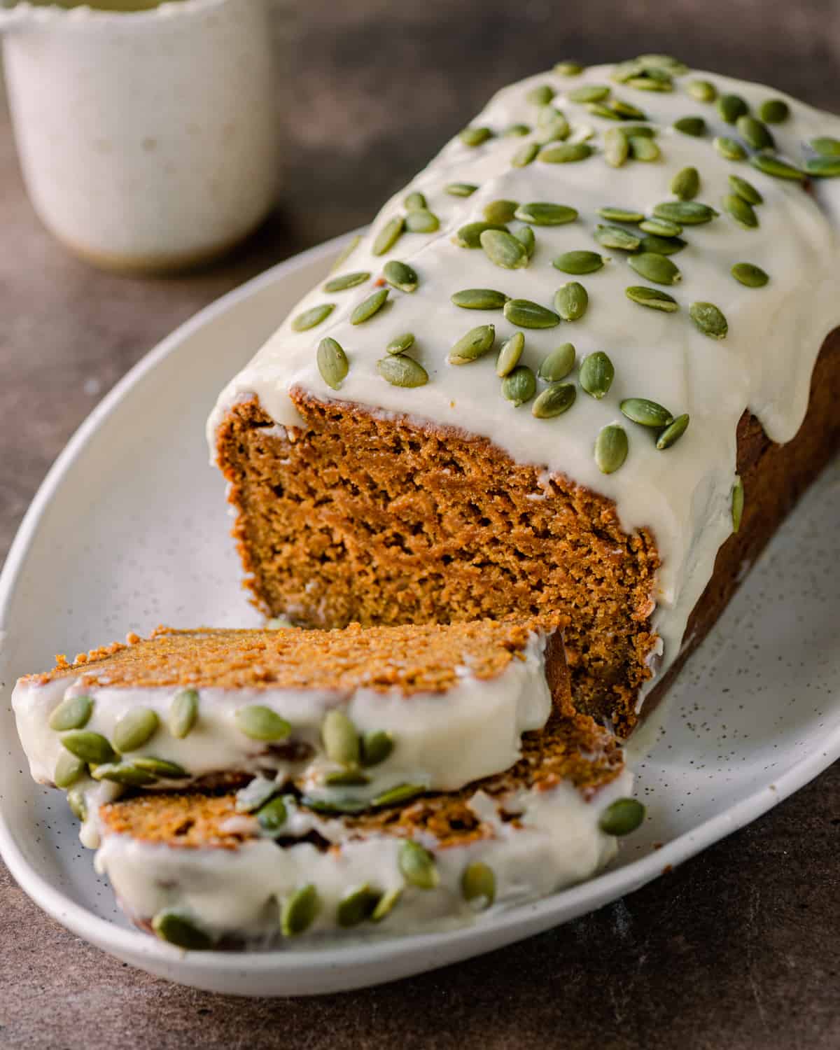 vegan pumpkin bread with cream cheese icing and pumpkin seeds sitting on white platter.
