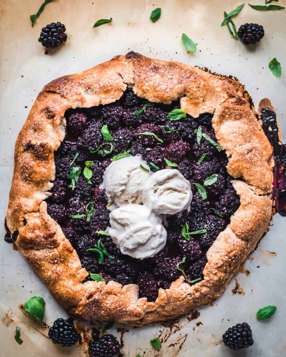 Cooked blackberry galette with mint, basil and ice cream on a baking sheet.