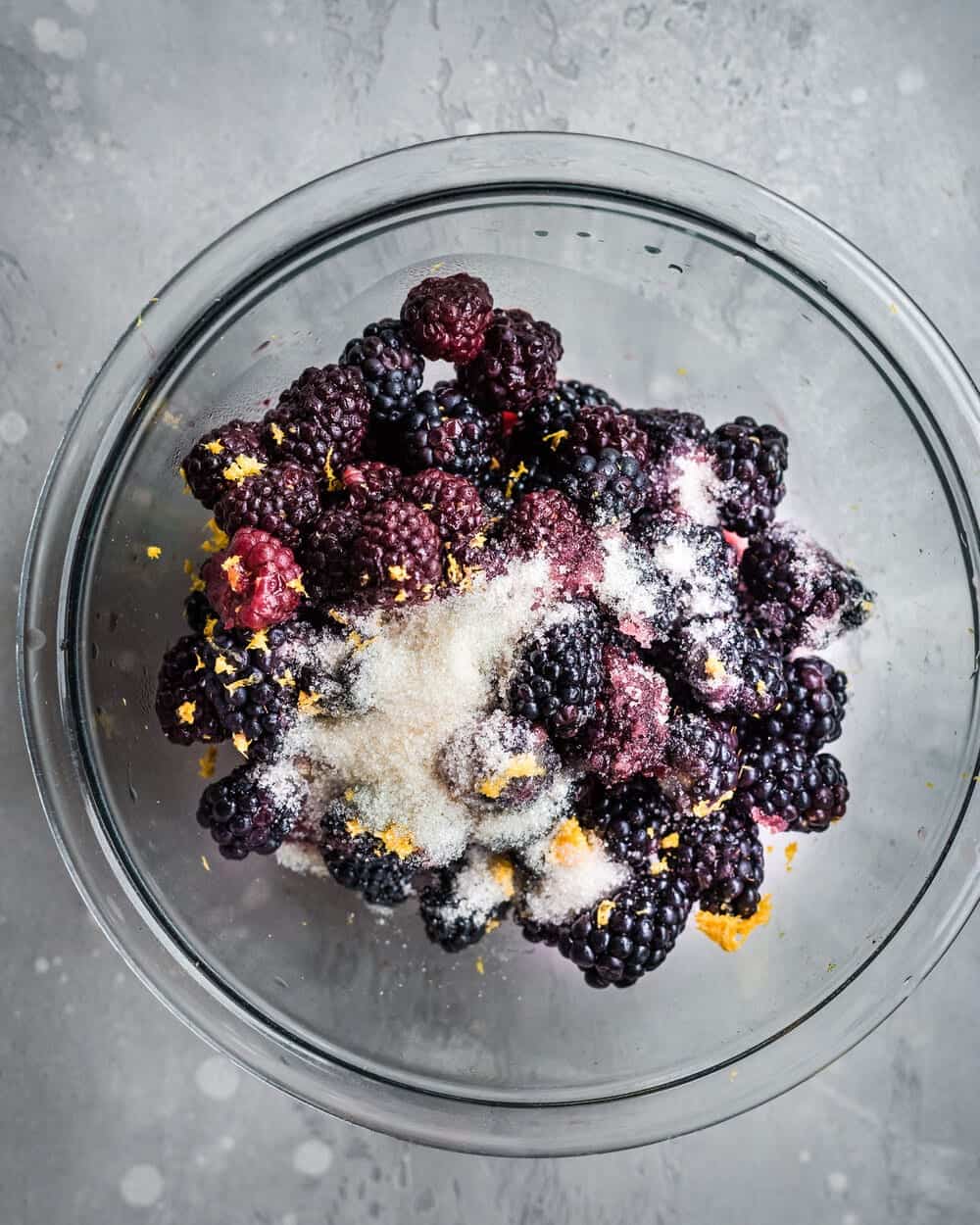 Blackberries, sugar and zest in a glass bowl.
