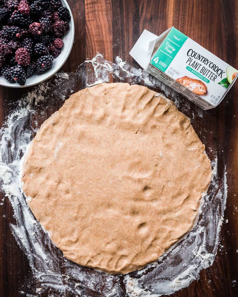Galette dough on a floured wooden cutting board next to a bowl of blackberries.