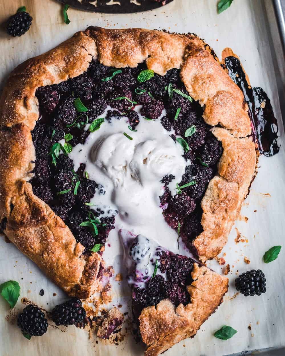 One slice cut out of cooked blackberry galette with mint, basil and melty ice cream.