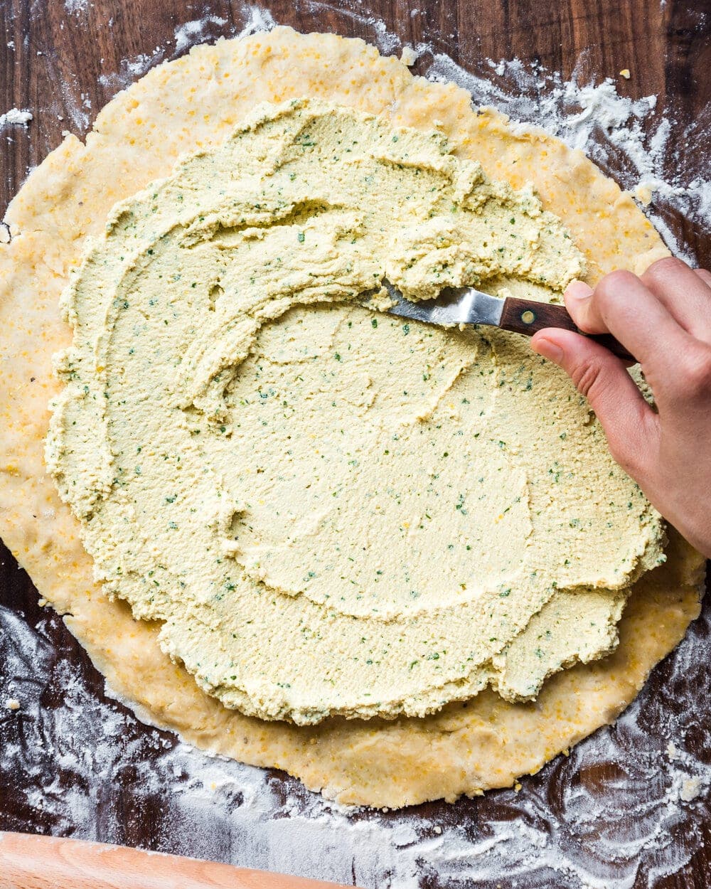 Person almost done spreading the ricotta over the dough.