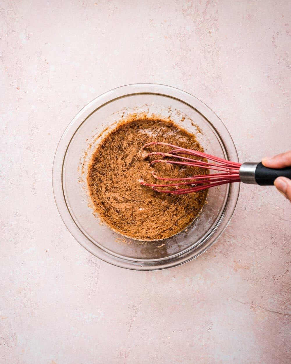 person whisking wet ingredients in a glass bowl.