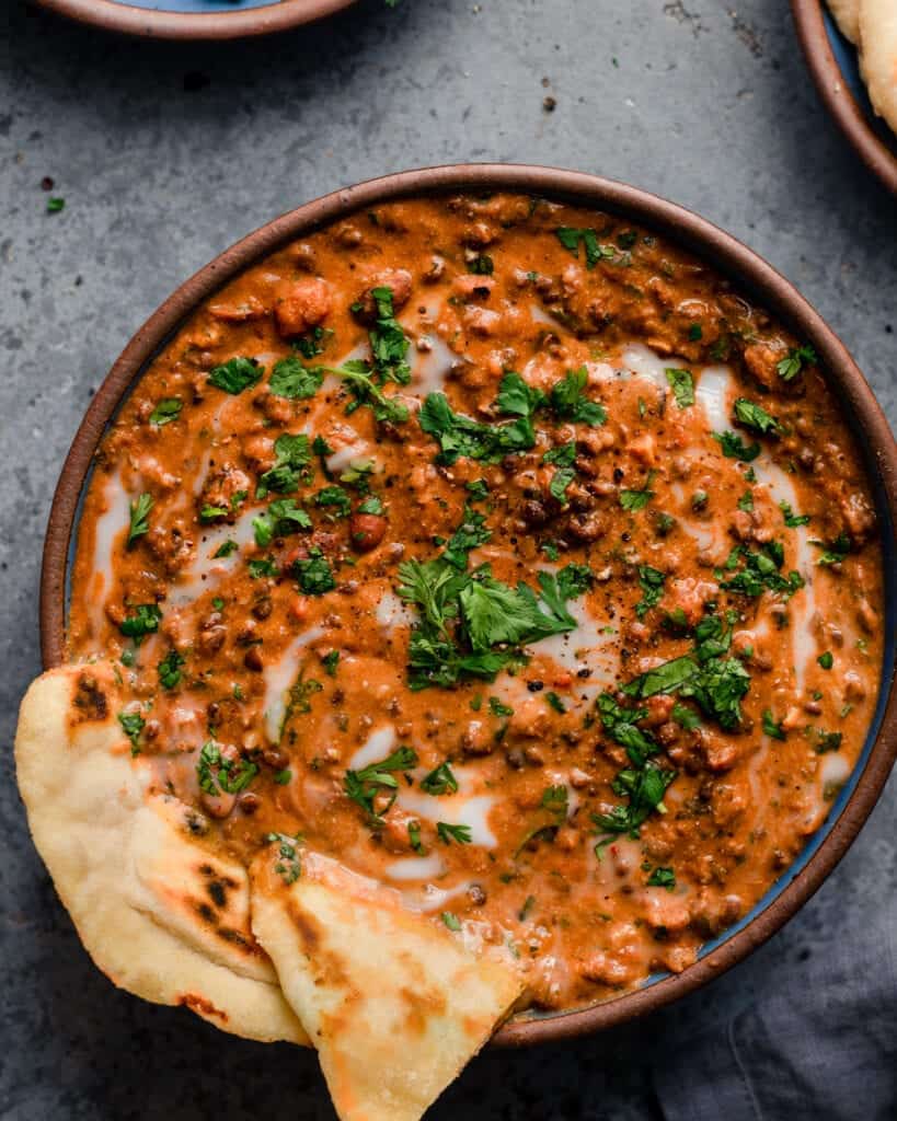 bowl of creamy vegan dal makhani with naan on blue background