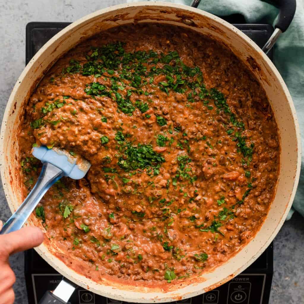 stirring cilantro into vegan dal makhani in saute pan