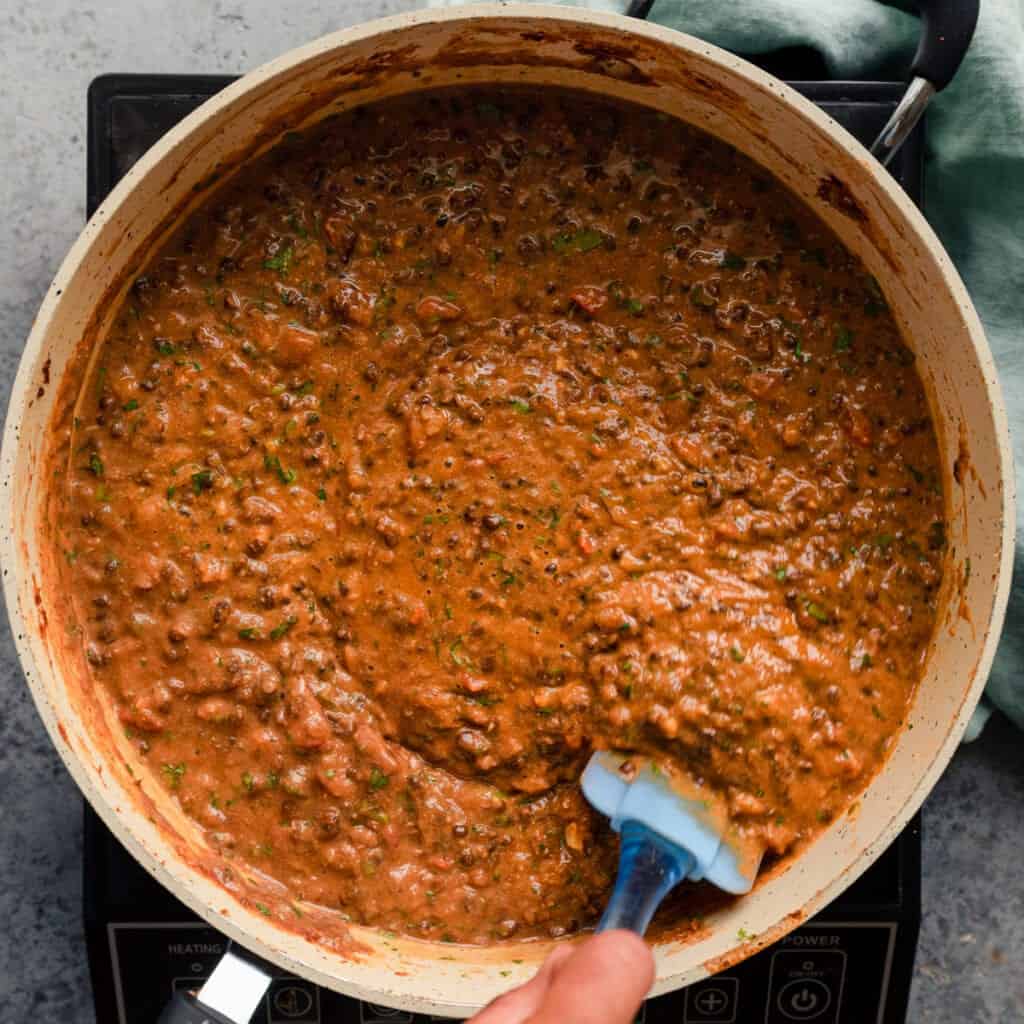 stirring creamy vegan Indian lentils in a saute pan