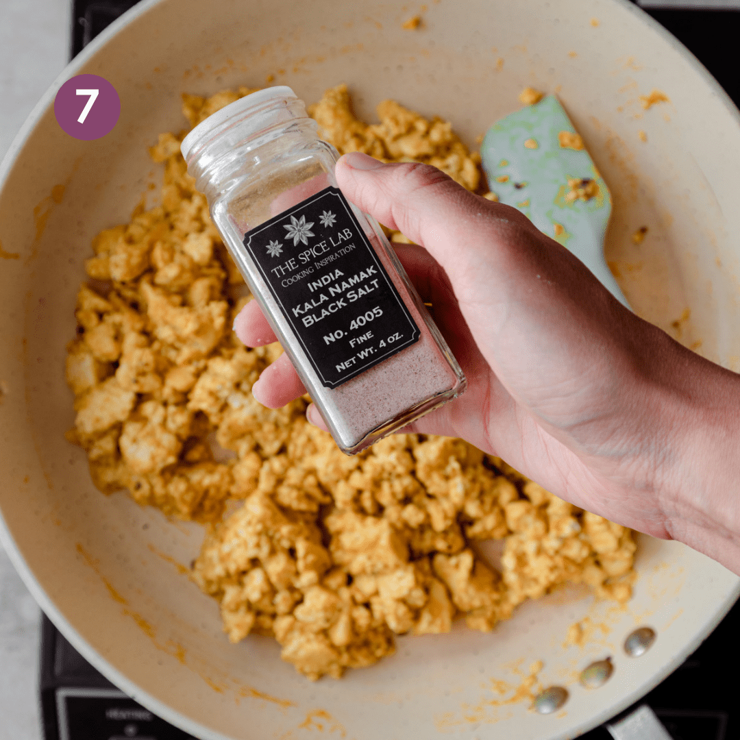 person holding a jar of kala namak over tofu scramble in skillet.