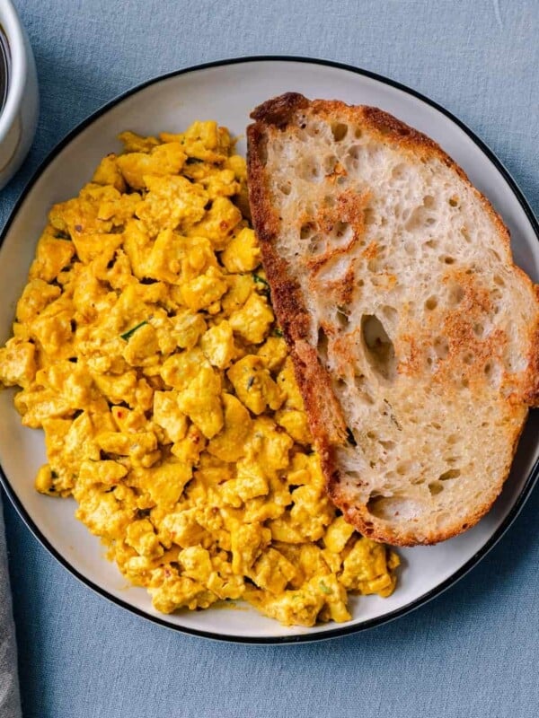tofu scramble with toast on a plate next to a cup of coffee.