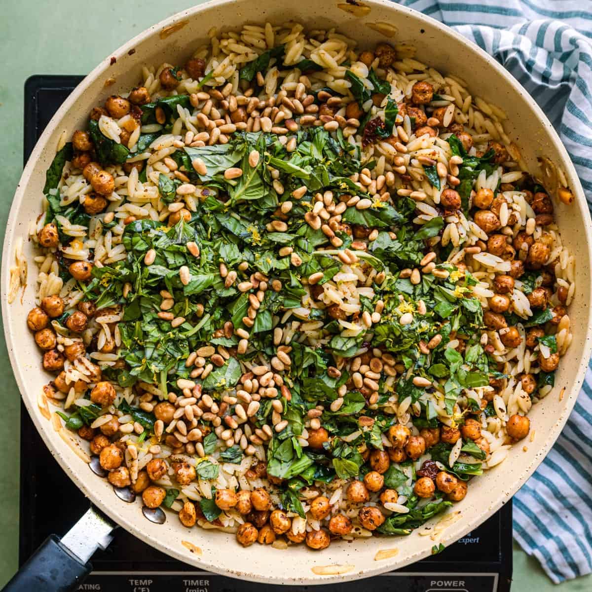 lemon orzo pasta salad in saute pan with fresh basil and toasted pine nuts on top.