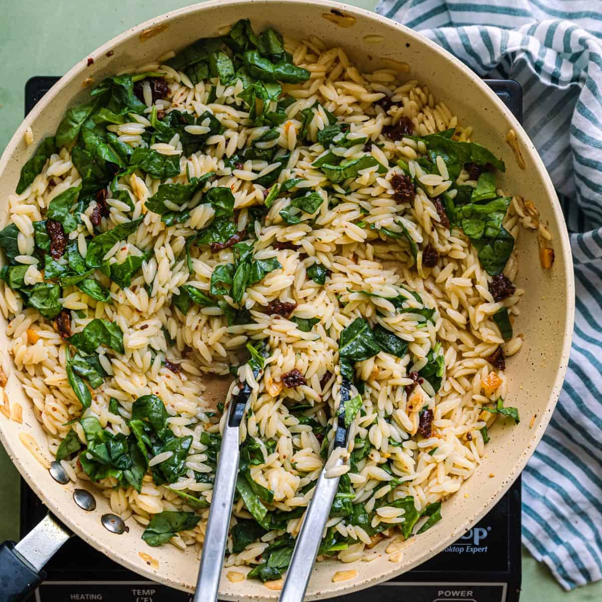 tongs tossing spinach into orzo pasta salad.