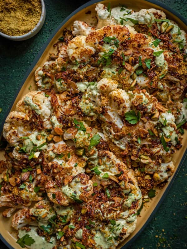 roasted cauliflower steaks with caramelized shallots and tahini sauce on yellow tray