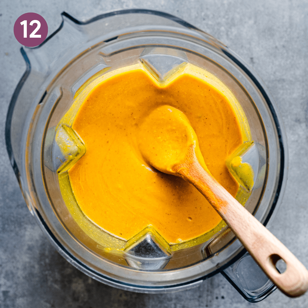 a creamy and velvety golden coconut milk soup in a blender with a wooden spoon digging in.