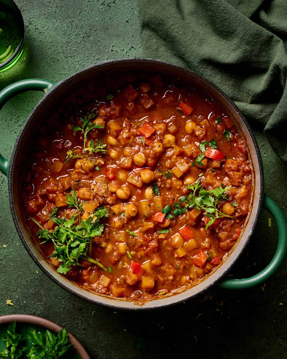 vegan tagine with chickpeas in a green dutch oven, garnished with parsley, on a green table.