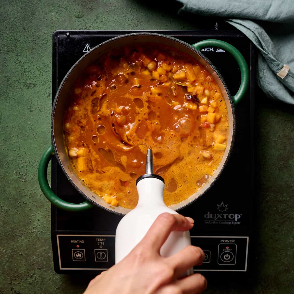 Person stirring vegan tagine in a dutch oven.