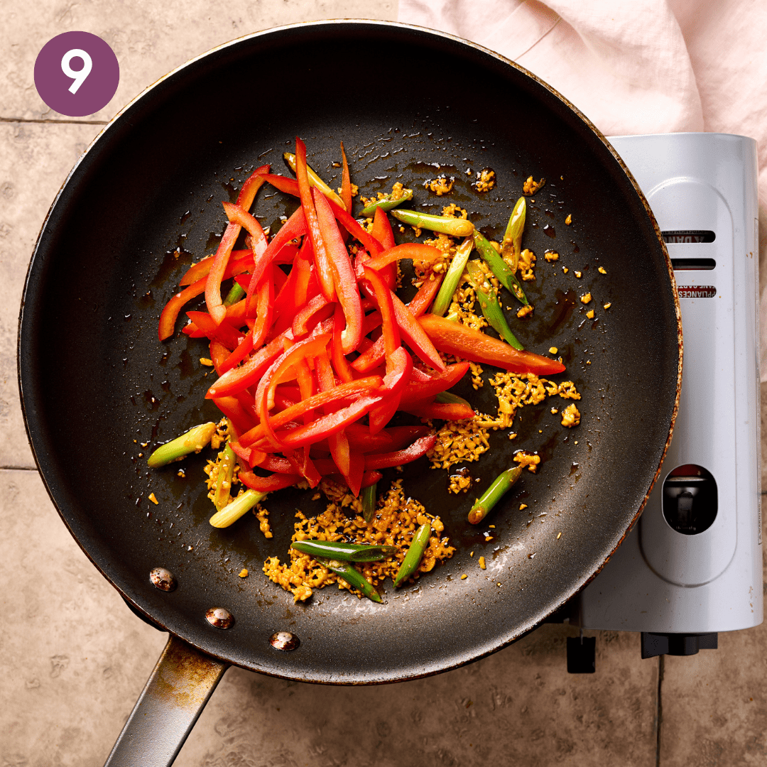 Fresh vegetables being added to cooked aromatics in pan.