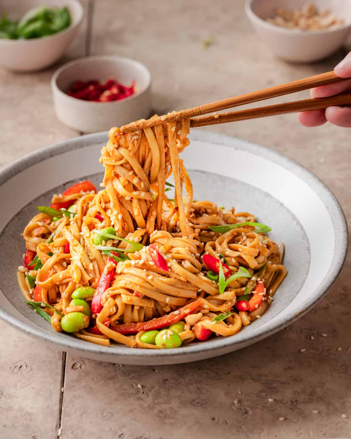 person using chopsticks to pick up sesame noodles from a bowl.