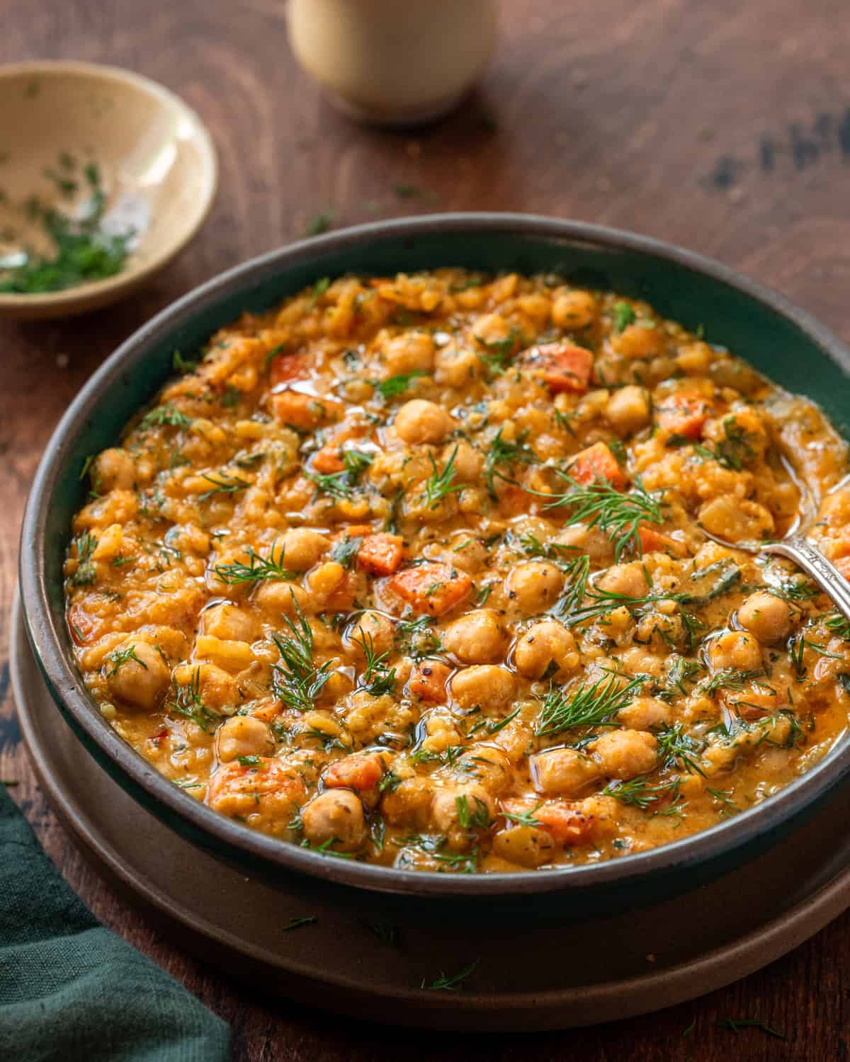chickpea soup with carrots and dill in a green bowl on a wooden table.