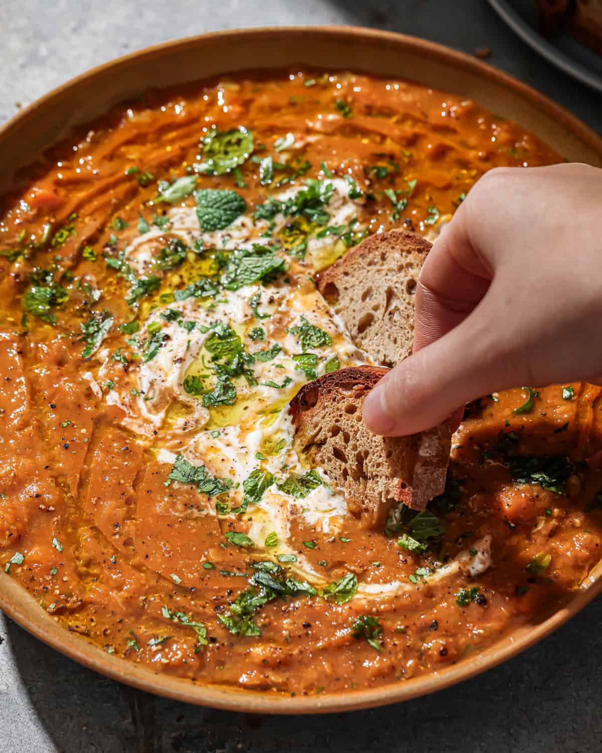 person dipping bread into a bowl of red lentil soup.