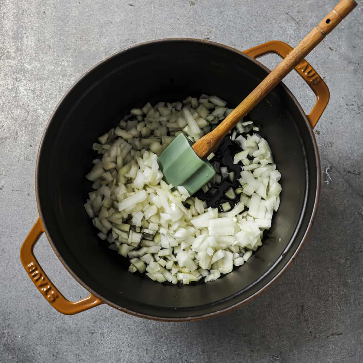 onions, olive oil and salt in a stockpot with a silicone spatula in it.