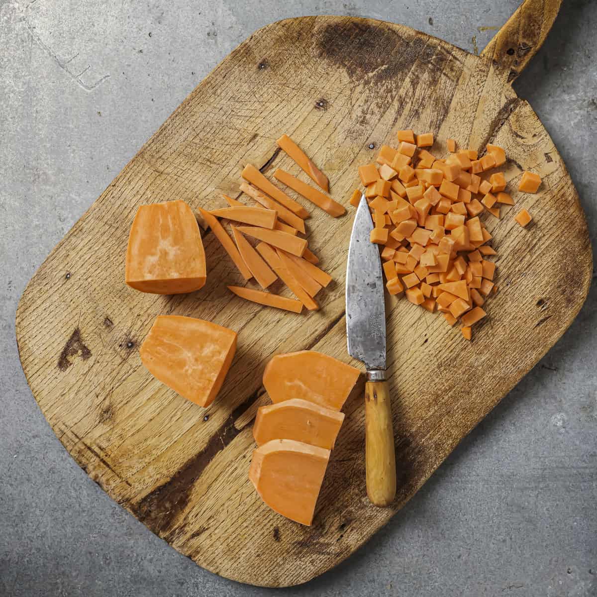 knife and chopped sweet potatoes on a wooden cutting board.