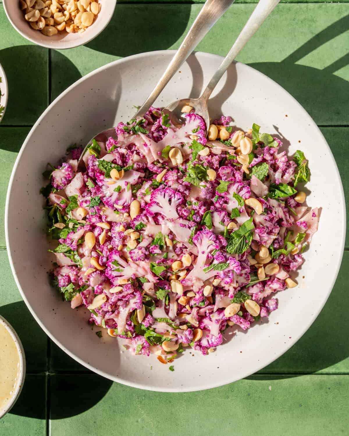 two servings spoons in a bowl of cauliflower salad on a table.
