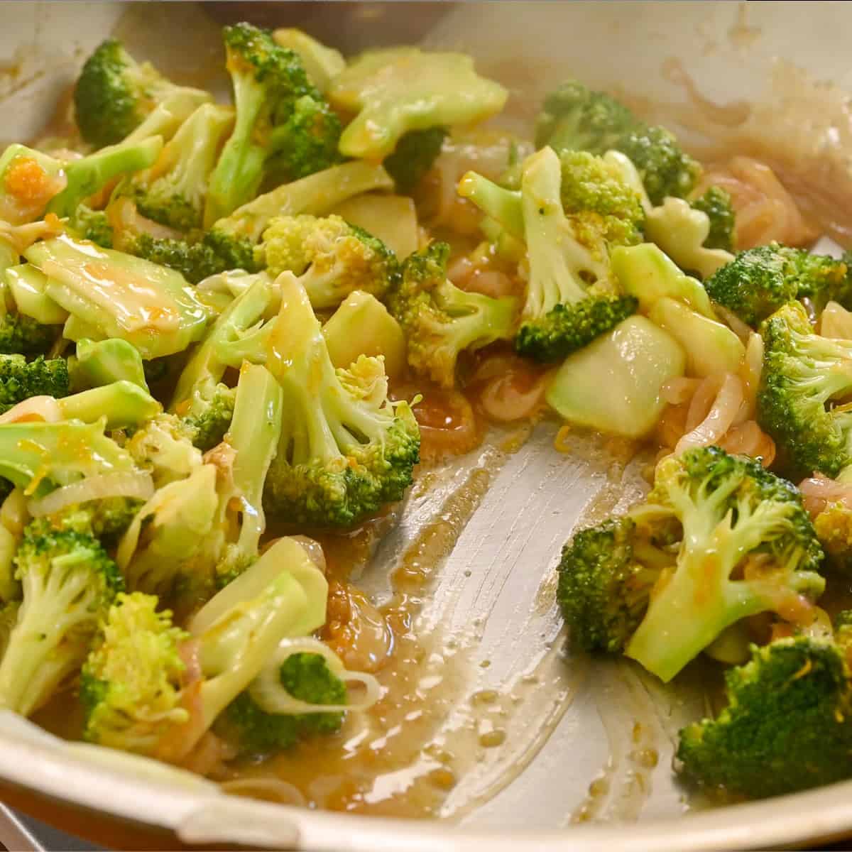 Broccoli coated in the orange sauce mixture in the frying pan.